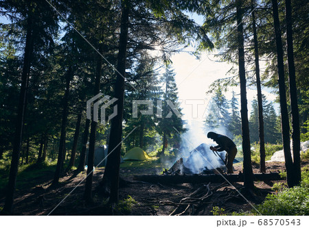 Tourist making fire near tents in forest. Tourist making fire near tents in forest. 68570543