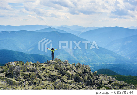 Rear view girl is opening her arms standing on top of cliff with powerful view mountain valley Rear view girl is opening her arms standing on top of cliff with powerful view mountain valley 68570544