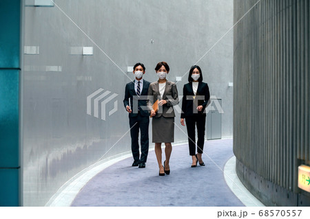 オフィスの廊下を歩くマスクをしたスーツ姿の男女のビジネスチーム 68570557