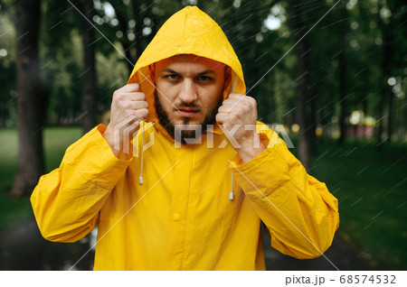 Man in raincoat puts on a hood in rainy day 68574532
