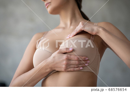 Young woman in beige brassier examining her breast 68576654