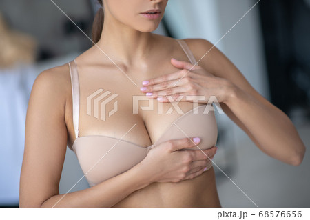Woman in beige brassier examining her breast 68576656
