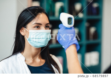 Young women getting body temperature control at enter of beauty salon Young women getting body temperature control at enter of beauty salon 68579897