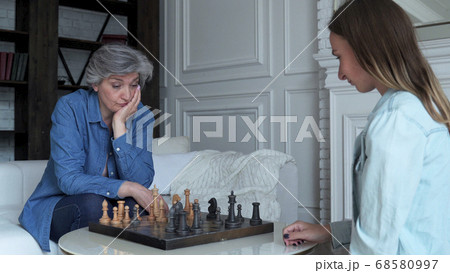 Mother and daughter play chess sitting on the sofa in the living room Mother and daughter play chess sitting on the sofa in the living room 68580997