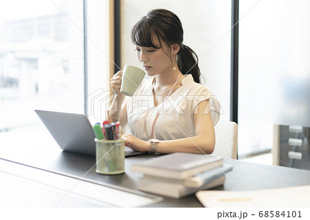 オフィスの窓際の席で飲み物をとりながらパソコン操作する女性 68584101