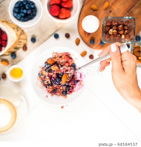Top view showing hands eating porridge with honey nuts, blueberries on white wooden table selective focus, blurred background Good morning - healthy breakfast background 68584537
