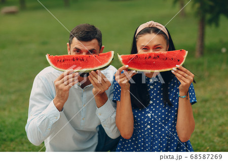 Young adult woman and man couple picnic at green grass meadow in park having fun and smile with watermelon 68587269
