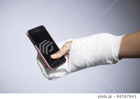 スマートフォンを持つ包帯を巻いた手 68587843