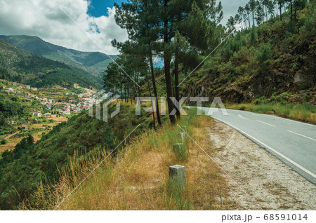 Road passing through hilly landscape and a village 68591014