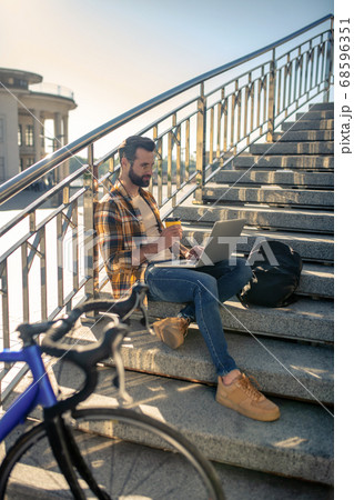 Man with laptop and coffee sitting on stairs near bike 68596351