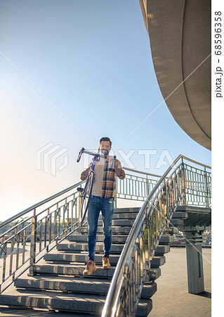 Smiling man carrying bike down city stairs 68596358