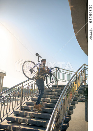 Young man carrying bicycle up the steps 68596359