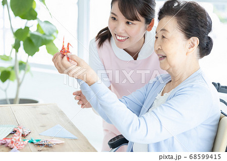 介護イメージ　折り紙を折るシニア女性と介護士 68599415