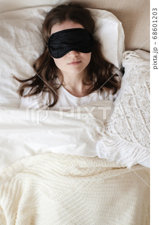 Young beautiful girl lying in comfortable bed wearing sleep mask in the morning at cozy room. Concept of rest at home, sleep, insomnia, self-isolation, stay home during quarantine, pandemic. Young beautiful girl lying in comfortable bed wearing sleep mask in the morning at cozy room. Concept of rest at home, sleep, insomnia, self-isolation, stay home during quarantine, pandemic. 68601203