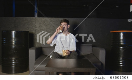 Young man eating popcorn and watching TV at home relaxing on couch 68601503