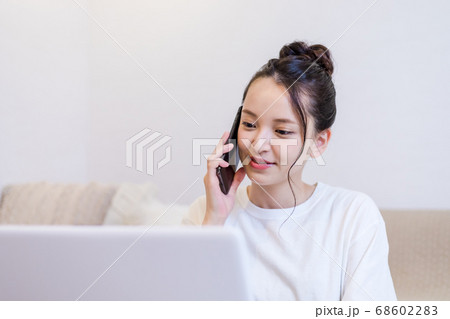 自宅でパソコンを見ながらスマホで会話する女性 68602283