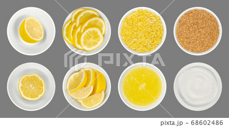 Fresh and processed lemons in white glass bowls, isolated over gray. Lemon halves, wedges and slices, freshly grated and dried lemon zest, juice and crystalline citric acid. Close up from above. Photo 68602486