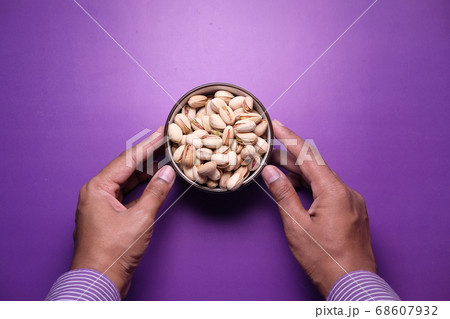 man hand holding a bowl salted pistachios nut on purple background man hand holding a bowl salted pistachios nut on purple background 68607932