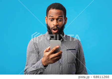 Surprised afro man using mobile phone on blue wall 68611260