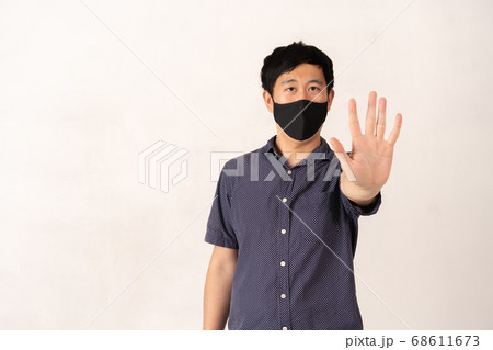 Asian man wearing face mask with hand palm raised towards camera 68611673
