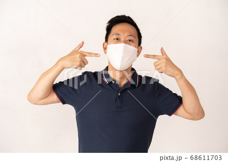 Asian man wearing face mask with hands pointing at face Asian man wearing face mask with hands pointing at face 68611703