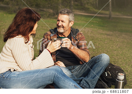 Middle-aged couple sitting on the grass in park and drinking tea. Middle-aged couple sitting on the grass in park and drinking tea. 68611807