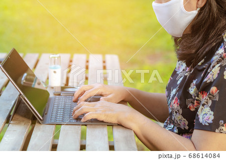 A quarantine woman wear a protective mask to prevent the spread of  of the Corona virus (Covid-19) ,Use a laptop to work from home with green lawn and garden. New normal concept.Selective focus 68614084
