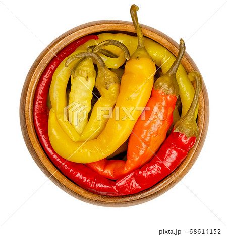Peperoni pickles in a wooden bowl. Pickled whole chili peppers of different bright colors. Vegetable, preserved in brine. Capsicum. Close-up from above, on white background, isolated macro food photo. 68614152