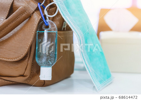 Mini portable alcohol gel bottle to kill Corona Virus(Covid-19) hang on a leather shoulder bag of a woman with a surgical mask on table at cafeteria.New normal lifestyle.Selective focus on alcohol gel 68614472
