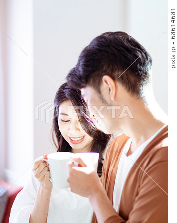 Young asian woman and man are enjoying spending time together at home with cup of coffee in hands. 68614681