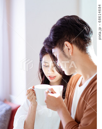 Young asian woman and man are enjoying spending time together at home with cup of coffee in hands. Young asian woman and man are enjoying spending time together at home with cup of coffee in hands. 68614684