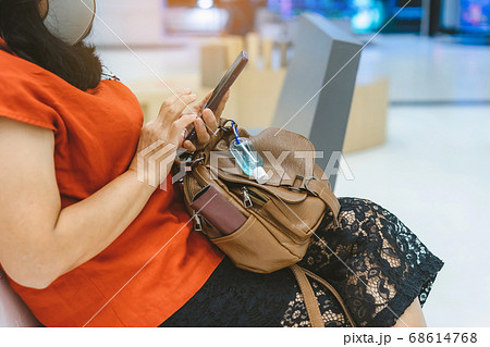 Mini alcohol gel bottle to kill Corona Virus(Covid-19) hang on a leather shoulder bag of a woman wearing a mask while use smartphone with alternative seating mark for social distancing in the mall. Mini alcohol gel bottle to kill Corona Virus(Covid-19) hang on a leather shoulder bag of a woman wearing a mask while use smartphone with alternative seating mark for social distancing in the mall. 68614768