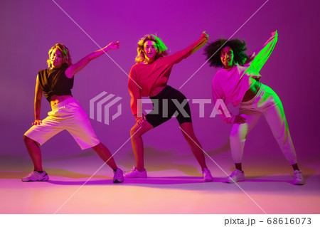 Sportive girls dancing hip-hop in stylish clothes on gradient background at dance hall in neon light 68616073
