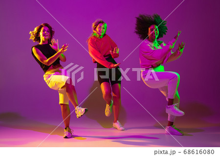 Sportive girls dancing hip-hop in stylish clothes on gradient background at dance hall in neon light 68616080