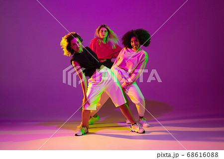 Sportive girls dancing hip-hop in stylish clothes on gradient background at dance hall in neon light Sportive girls dancing hip-hop in stylish clothes on gradient background at dance hall in neon light 68616088