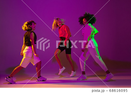 Sportive girls dancing hip-hop in stylish clothes on gradient background at dance hall in neon light Sportive girls dancing hip-hop in stylish clothes on gradient background at dance hall in neon light 68616095