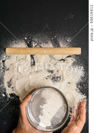 Males hands with flour sift flour with a sieve for making dough, topview. on black background. vertical photo Males hands with flour sift flour with a sieve for making dough, topview. on black background. vertical photo 68616812