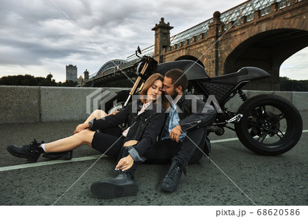Beautiful biker couple in love are sitting on the road next to motorcycles in the city 68620586