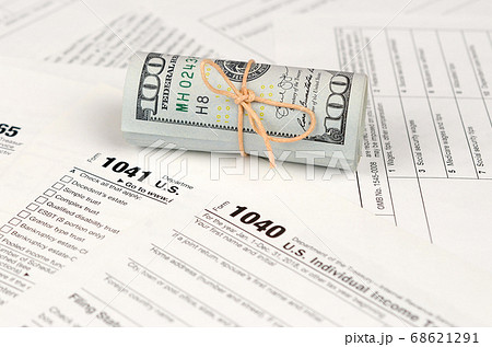 Tax forms lies near roll of hundred dollar bills. 68621291