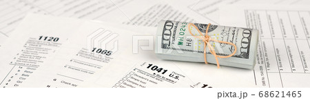 Tax forms lies near roll of hundred dollar bills. Tax forms lies near roll of hundred dollar bills. 68621465
