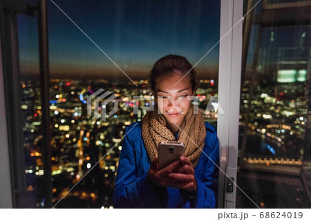 London urban people city lifestyle woman using phone app texting sms on social media. Young Asian girl holding cellphone at night on skyline background London urban people city lifestyle woman using phone app texting sms on social media. Young Asian girl holding cellphone at night on skyline background 68624019