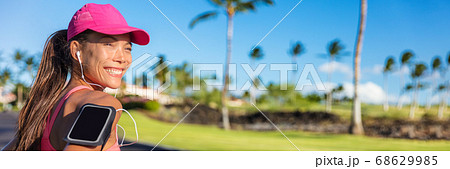 Fitness summer motivation running music woman runner run banner. Jogging Asian girl listening to smartphone app with earphones wearing cap and armband smart phone holder. Horizontal panorama crop 68629985