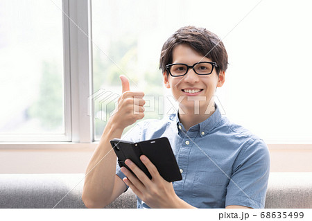 ソファーでスマホをみる男性(サムアップ) 68635499