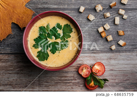 Pumpkin cream soup in bowl with parsley on wooden table with crackers and tomatoes. Traditional autumn food for Halloween Pumpkin cream soup in bowl with parsley on wooden table with crackers and tomatoes. Traditional autumn food for Halloween 68635759