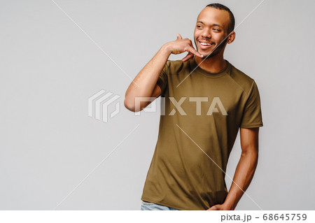 Handsome young African American man showing a call me sign and smiling while standing isolated on grey background Handsome young African American man showing a call me sign and smiling while standing isolated on grey background 68645759