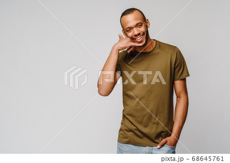 Handsome young African American man showing a call me sign and smiling while standing isolated on grey background Handsome young African American man showing a call me sign and smiling while standing isolated on grey background 68645761