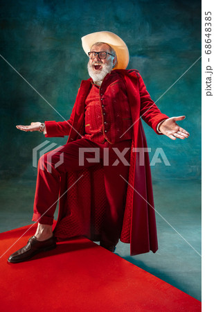 Modern stylish Santa Claus in red fashionable suit and cowboy's hat on dark background Modern stylish Santa Claus in red fashionable suit and cowboy's hat on dark background 68648385