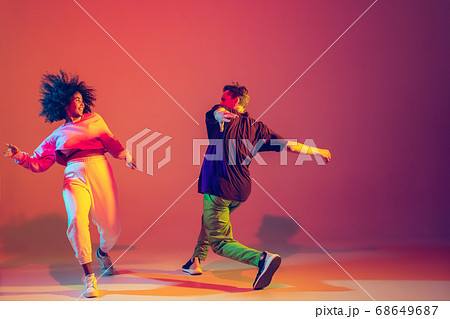 Stylish man and woman dancing hip-hop in bright clothes on gradient background at dance hall in neon light Stylish man and woman dancing hip-hop in bright clothes on gradient background at dance hall in neon light 68649687