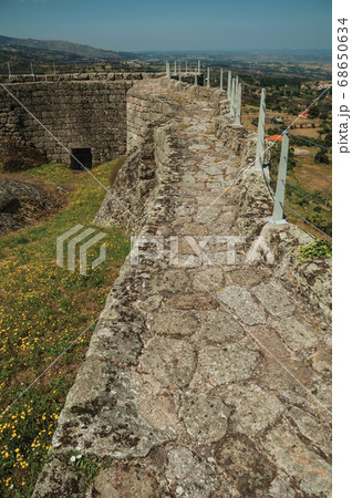 Pathway over stone wall around flowered courtyard 68650634