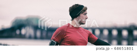 Winter runner man in cold outdoor air training cardio. Male runner stretching after running in fall weather wearing warm sport running clothing. Handsome male fitness sport model outdoors. Panoramic 68651801